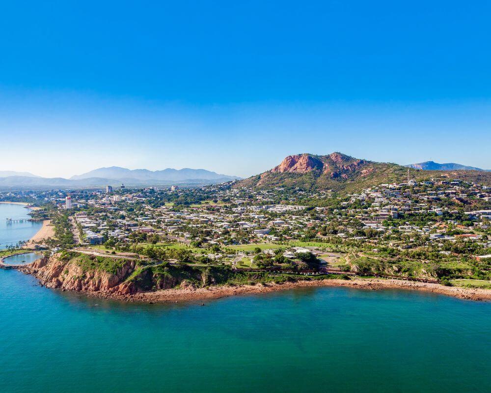 Aerial view of Townsville coastline with rocky shore, urban area, and Castle Hill in the background.